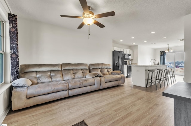 living room featuring ceiling fan, a textured ceiling, and light wood-type flooring