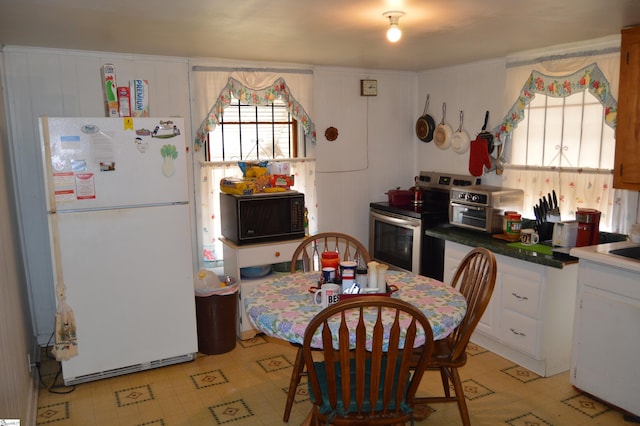 kitchen featuring a healthy amount of sunlight, stainless steel range with electric cooktop, white fridge, and white cabinets