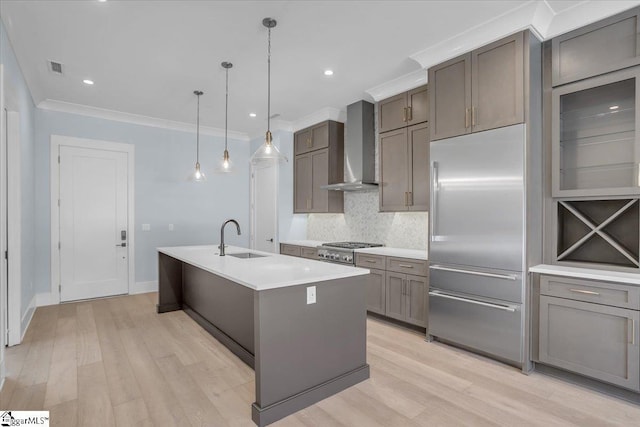 kitchen featuring sink, appliances with stainless steel finishes, an island with sink, pendant lighting, and wall chimney range hood