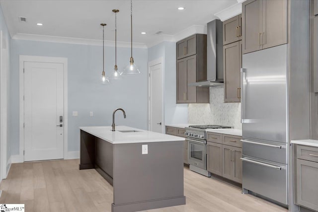 kitchen with sink, premium appliances, hanging light fixtures, a center island with sink, and wall chimney exhaust hood