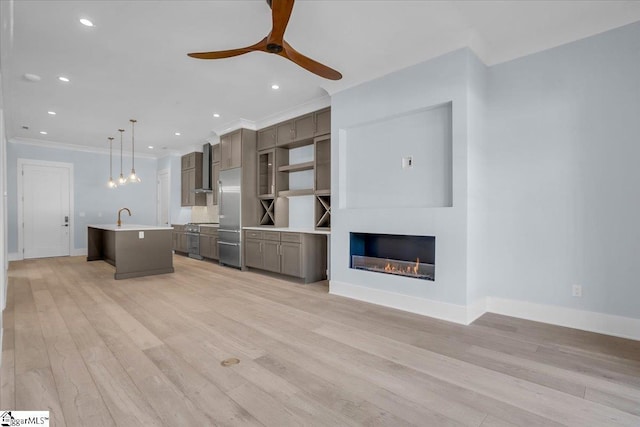 unfurnished living room with sink, crown molding, ceiling fan, and light wood-type flooring