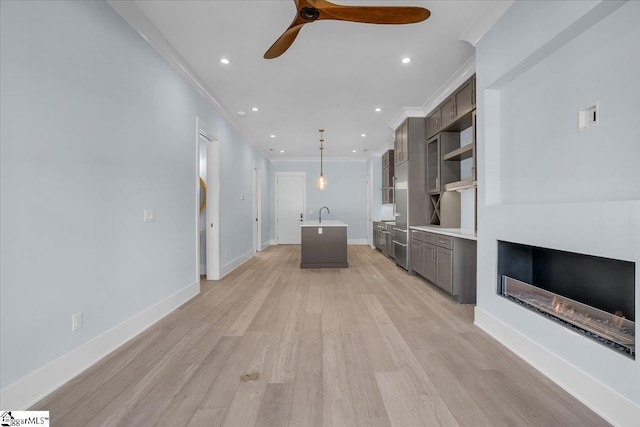 unfurnished living room with crown molding, ceiling fan, sink, and light wood-type flooring