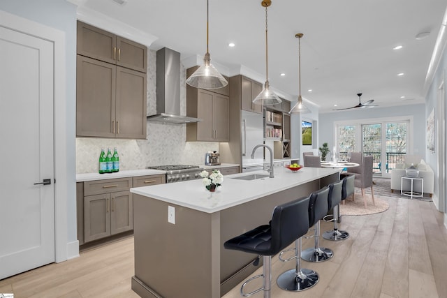 kitchen featuring an island with sink, sink, hanging light fixtures, wall chimney exhaust hood, and light hardwood / wood-style flooring