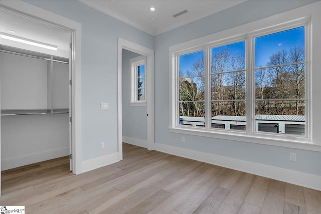 unfurnished bedroom with multiple windows, light wood-type flooring, and a closet