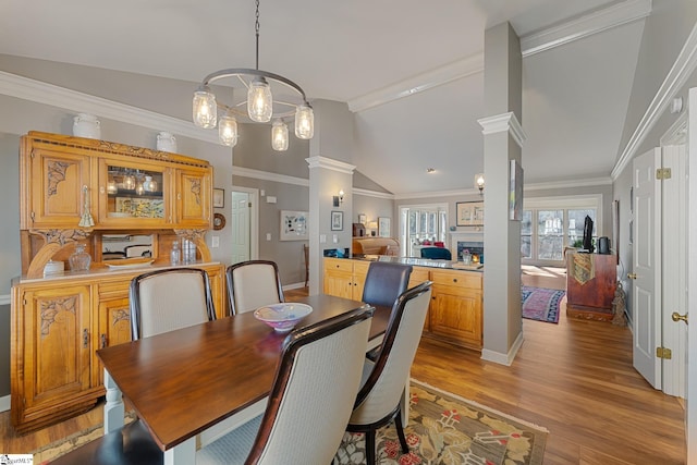 dining space featuring crown molding, light hardwood / wood-style flooring, vaulted ceiling, and ornate columns