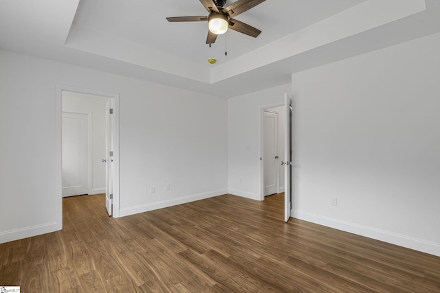 empty room with a raised ceiling, dark hardwood / wood-style floors, and ceiling fan