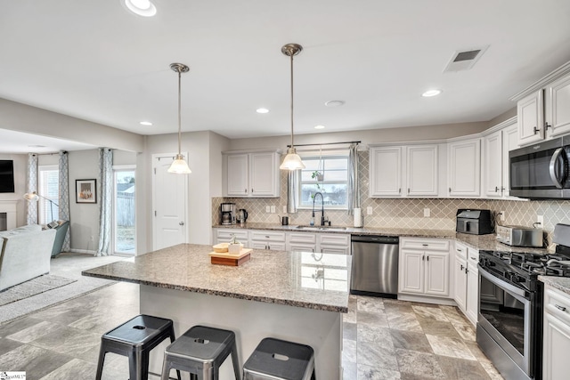 kitchen with stainless steel appliances, white cabinetry, sink, and decorative light fixtures