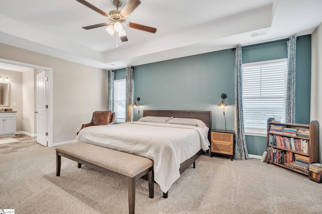 bedroom with ensuite bathroom, carpet, ceiling fan, and a tray ceiling