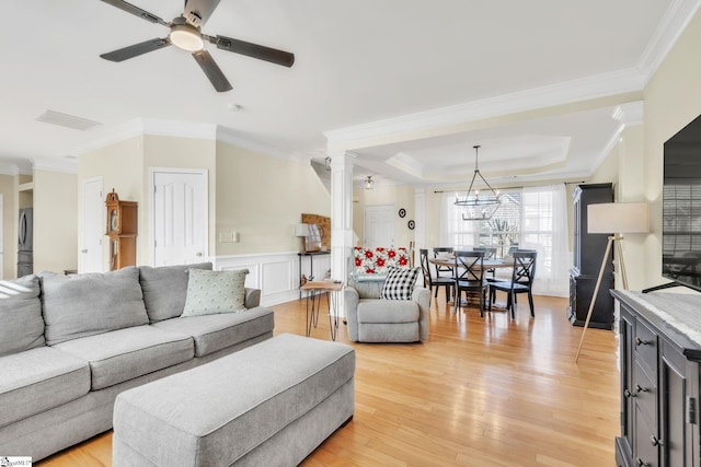 living room with a tray ceiling, ceiling fan with notable chandelier, light hardwood / wood-style flooring, and crown molding