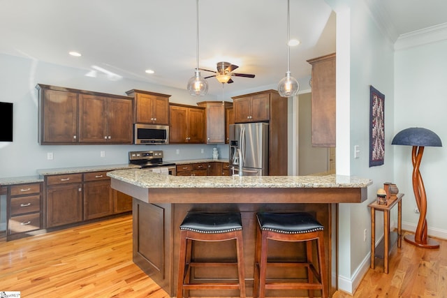 kitchen with a breakfast bar area, light wood-type flooring, appliances with stainless steel finishes, kitchen peninsula, and pendant lighting