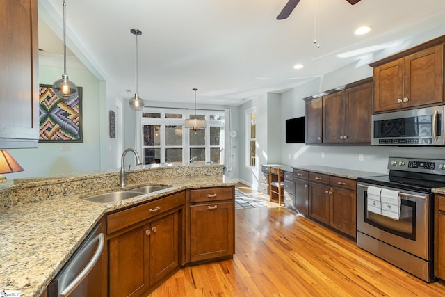 kitchen featuring sink, hanging light fixtures, stainless steel appliances, light stone counters, and light wood-type flooring