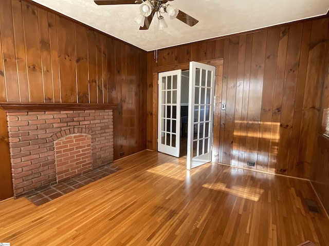 unfurnished living room with ceiling fan, wood walls, and light wood-type flooring