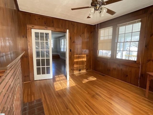 empty room with ceiling fan, hardwood / wood-style floors, wooden walls, and french doors