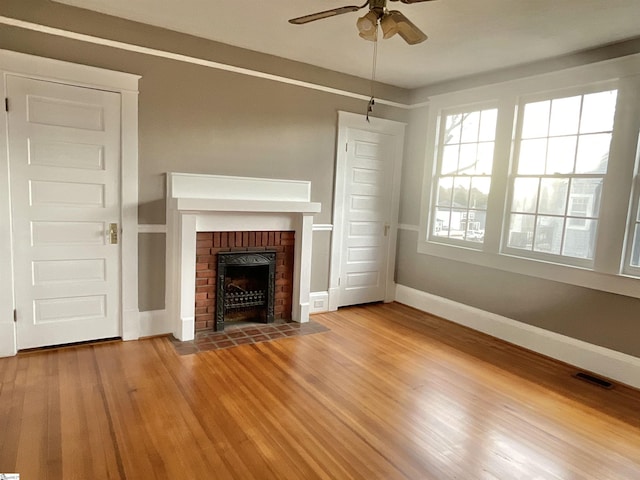 unfurnished living room with ceiling fan, hardwood / wood-style floors, and a brick fireplace