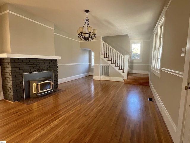 unfurnished living room with a notable chandelier, dark wood-type flooring, and a wood stove