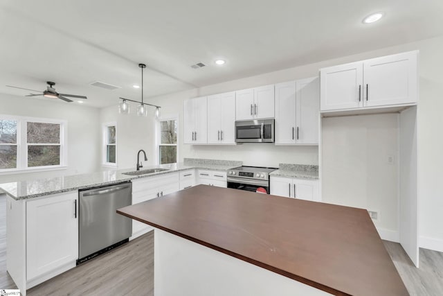 kitchen with appliances with stainless steel finishes, decorative light fixtures, white cabinetry, sink, and a center island