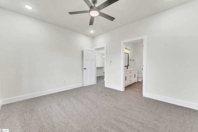 unfurnished bedroom featuring ensuite bathroom, sink, light colored carpet, and ceiling fan