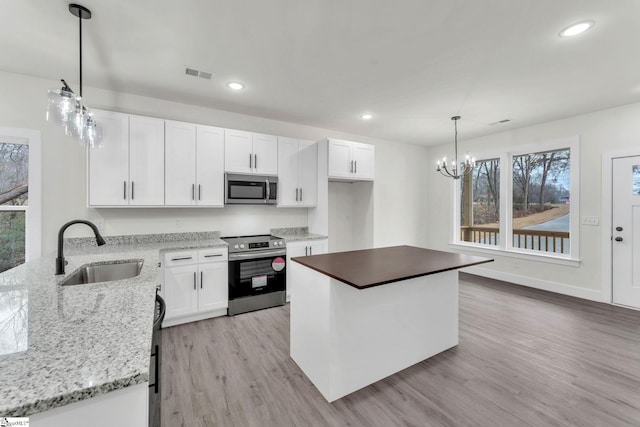 kitchen with sink, white cabinets, hanging light fixtures, stainless steel appliances, and light wood-type flooring