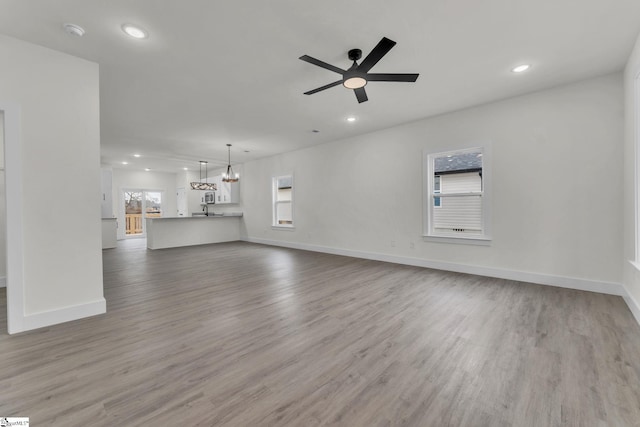 unfurnished living room with ceiling fan with notable chandelier and light hardwood / wood-style flooring