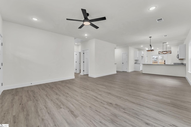 unfurnished living room featuring ceiling fan with notable chandelier and light wood-type flooring