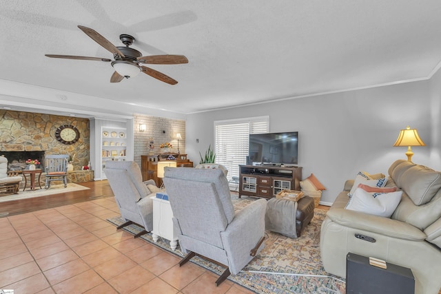 tiled living room featuring crown molding, a stone fireplace, ceiling fan, and a textured ceiling