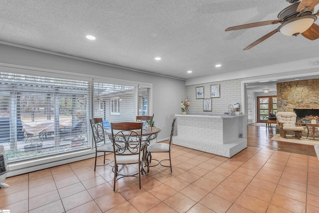 tiled dining room with ceiling fan, a stone fireplace, and a textured ceiling