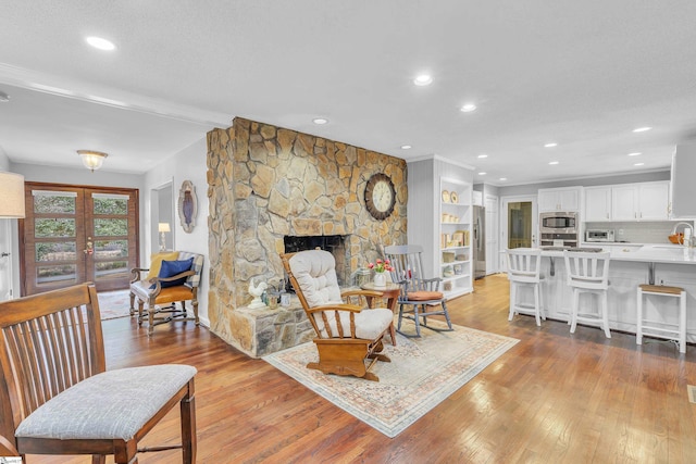 living room featuring french doors, a stone fireplace, sink, and light hardwood / wood-style flooring