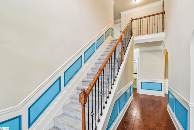 staircase featuring hardwood / wood-style flooring, crown molding, and a high ceiling