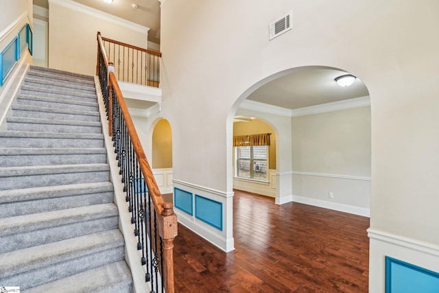 staircase with a high ceiling, ornamental molding, and wood-type flooring