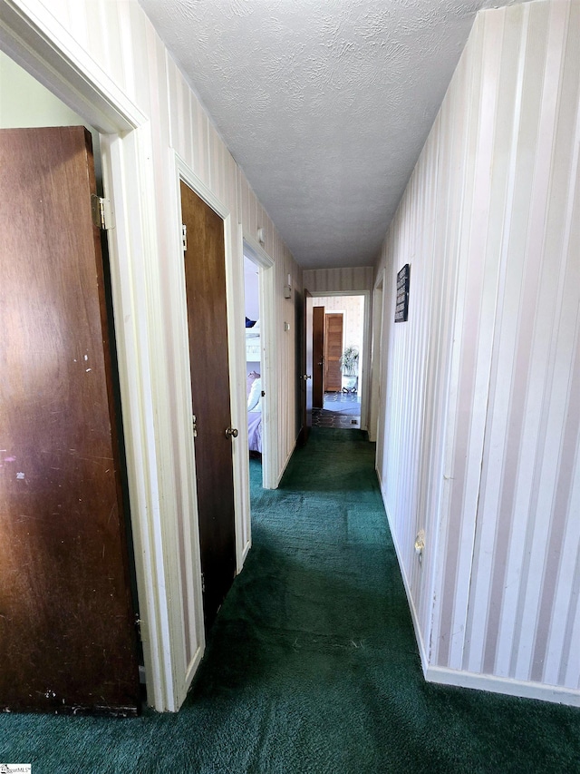 corridor featuring a textured ceiling and dark colored carpet