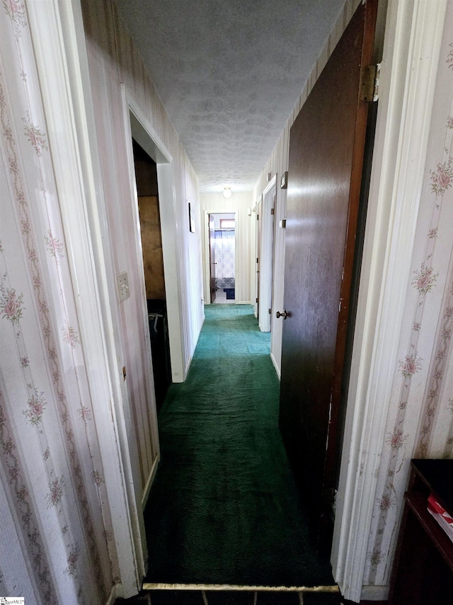 hallway with a textured ceiling and dark colored carpet