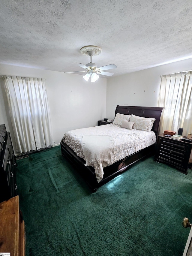 bedroom with ceiling fan, dark carpet, and a textured ceiling