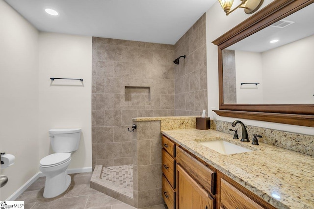 bathroom featuring tile patterned flooring, vanity, a tile shower, and toilet