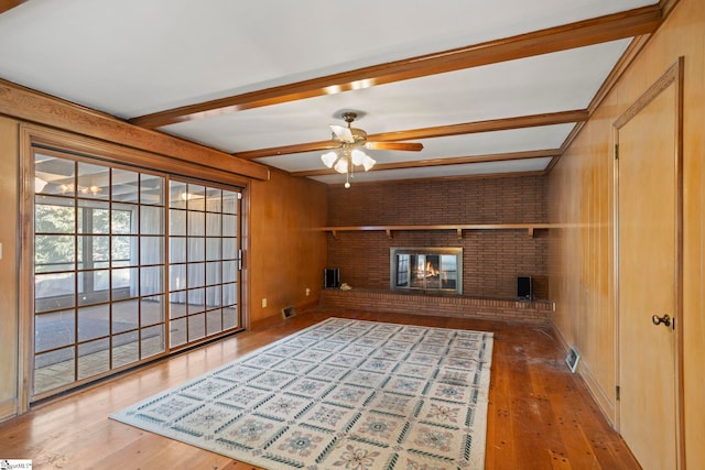 unfurnished room with ceiling fan, hardwood / wood-style floors, beam ceiling, wooden walls, and a fireplace