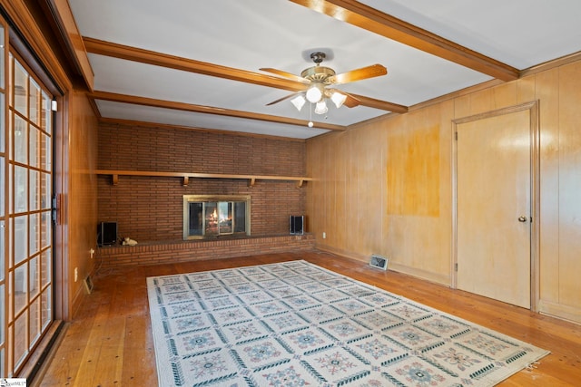 unfurnished living room featuring wooden walls, brick wall, a brick fireplace, beamed ceiling, and light wood-type flooring