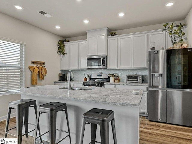 kitchen with sink, white cabinets, a kitchen bar, a kitchen island with sink, and stainless steel appliances