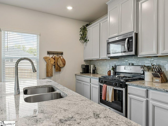 kitchen with sink, white cabinets, decorative backsplash, light stone counters, and stainless steel appliances