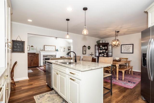 kitchen featuring decorative light fixtures, sink, light stone counters, stainless steel appliances, and a center island with sink