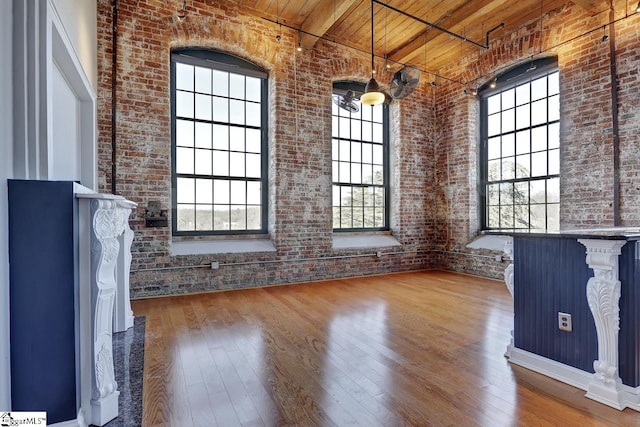 unfurnished living room featuring wood ceiling, brick wall, wood-type flooring, a healthy amount of sunlight, and a high ceiling