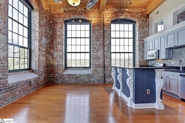 kitchen with a breakfast bar, appliances with stainless steel finishes, dark hardwood / wood-style floors, brick wall, and a high ceiling