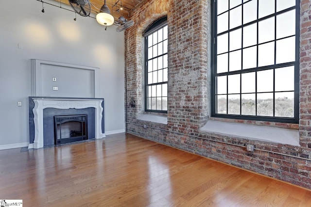 unfurnished living room featuring wood-type flooring, a healthy amount of sunlight, and brick wall