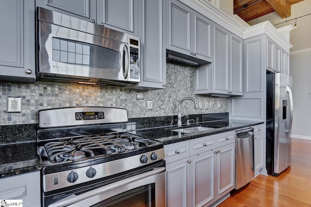 kitchen with appliances with stainless steel finishes, tasteful backsplash, sink, dark stone counters, and light hardwood / wood-style flooring