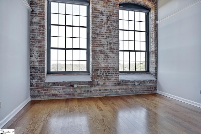 spare room featuring hardwood / wood-style flooring, brick wall, and plenty of natural light