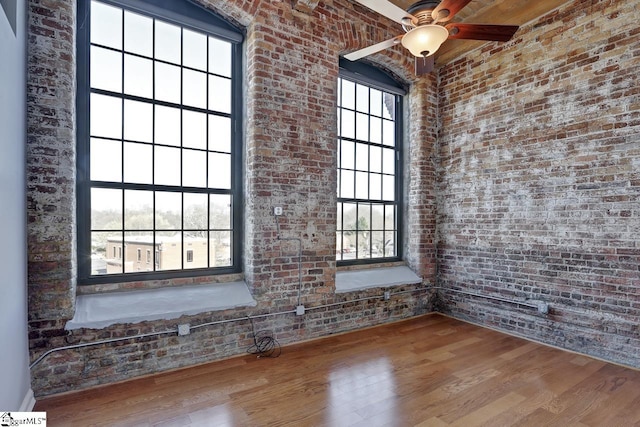 spare room featuring hardwood / wood-style flooring, brick wall, and a high ceiling