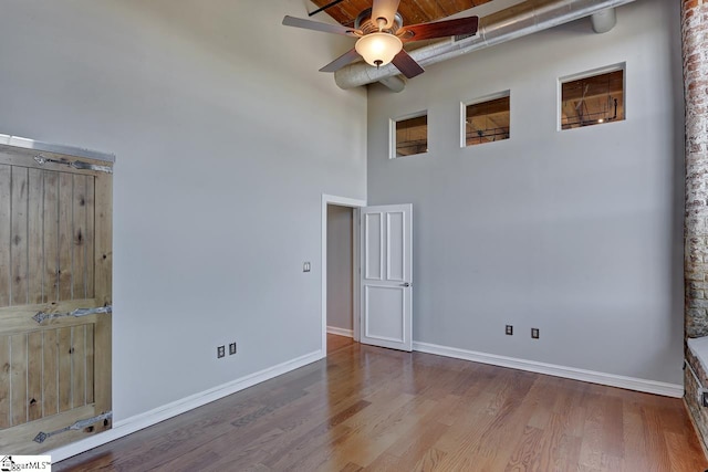 spare room featuring hardwood / wood-style flooring, ceiling fan, and a towering ceiling