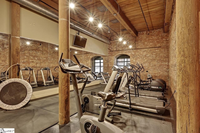 exercise room with brick wall, a towering ceiling, and wooden ceiling