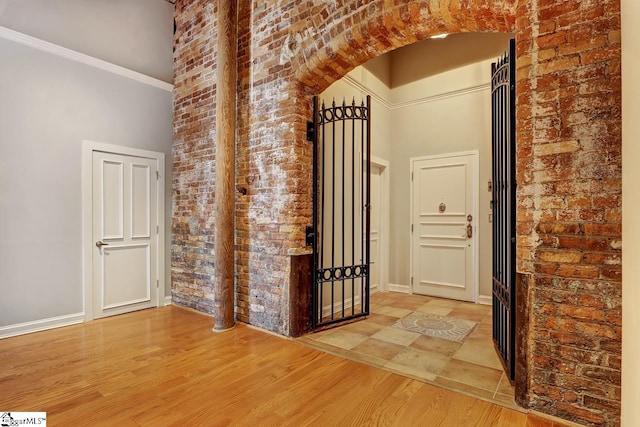 corridor with hardwood / wood-style flooring, ornamental molding, brick wall, and a towering ceiling