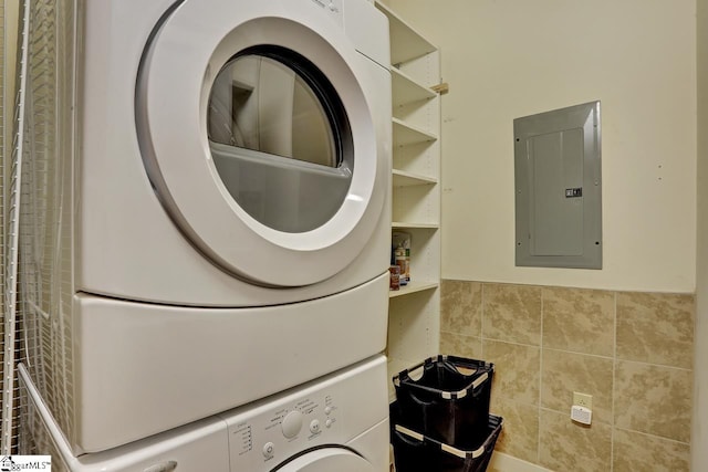 laundry room with tile walls, electric panel, and stacked washing maching and dryer