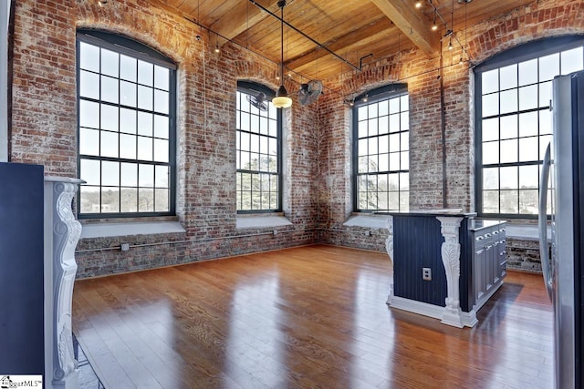 interior space with wood ceiling, dark wood-type flooring, a towering ceiling, brick wall, and beamed ceiling