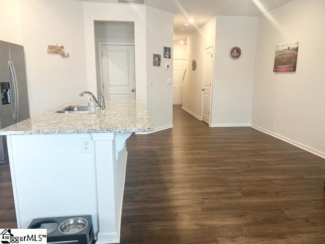 kitchen featuring sink, a kitchen island with sink, stainless steel refrigerator with ice dispenser, light stone countertops, and dark wood-type flooring